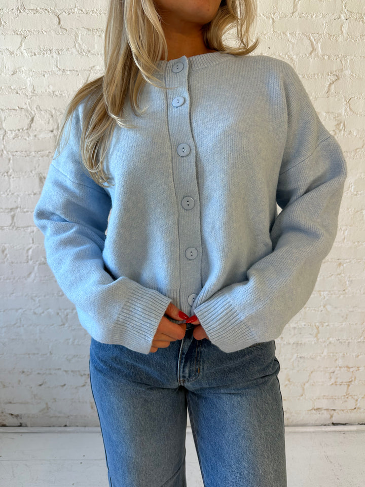 Woman wearing baby blue knit button down cardigan with medium wash wide leg jean. 