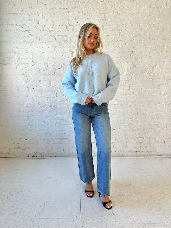Woman wearing baby blue knit button down cardigan with medium wash wide leg jean. 