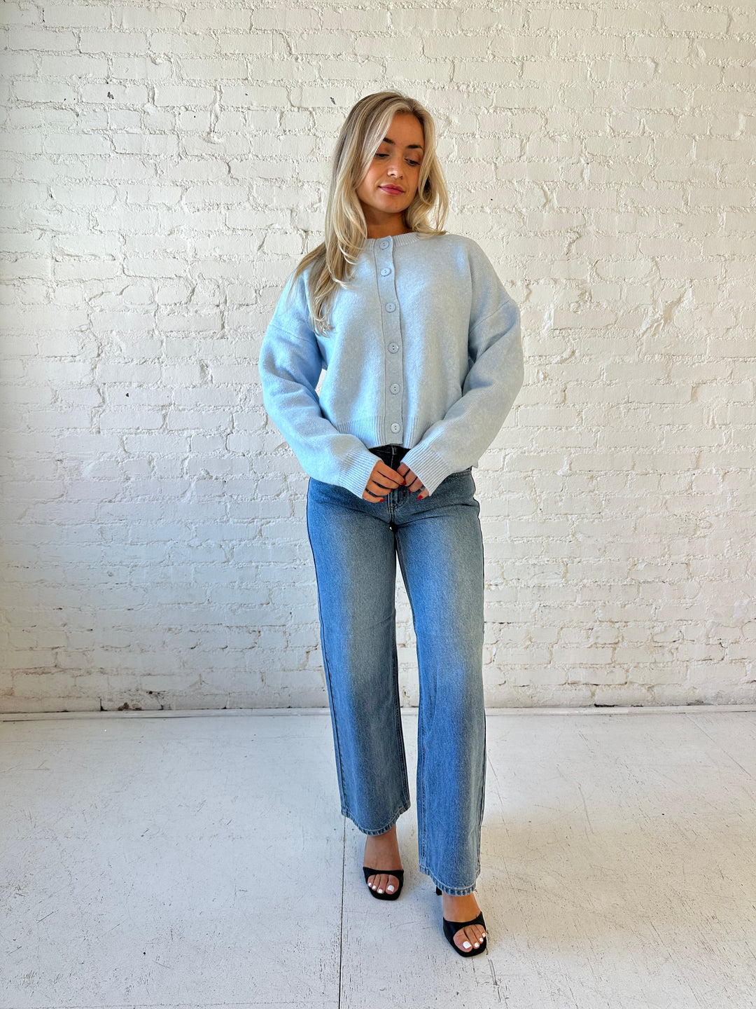 Woman wearing baby blue knit button down cardigan with medium wash wide leg jean. 