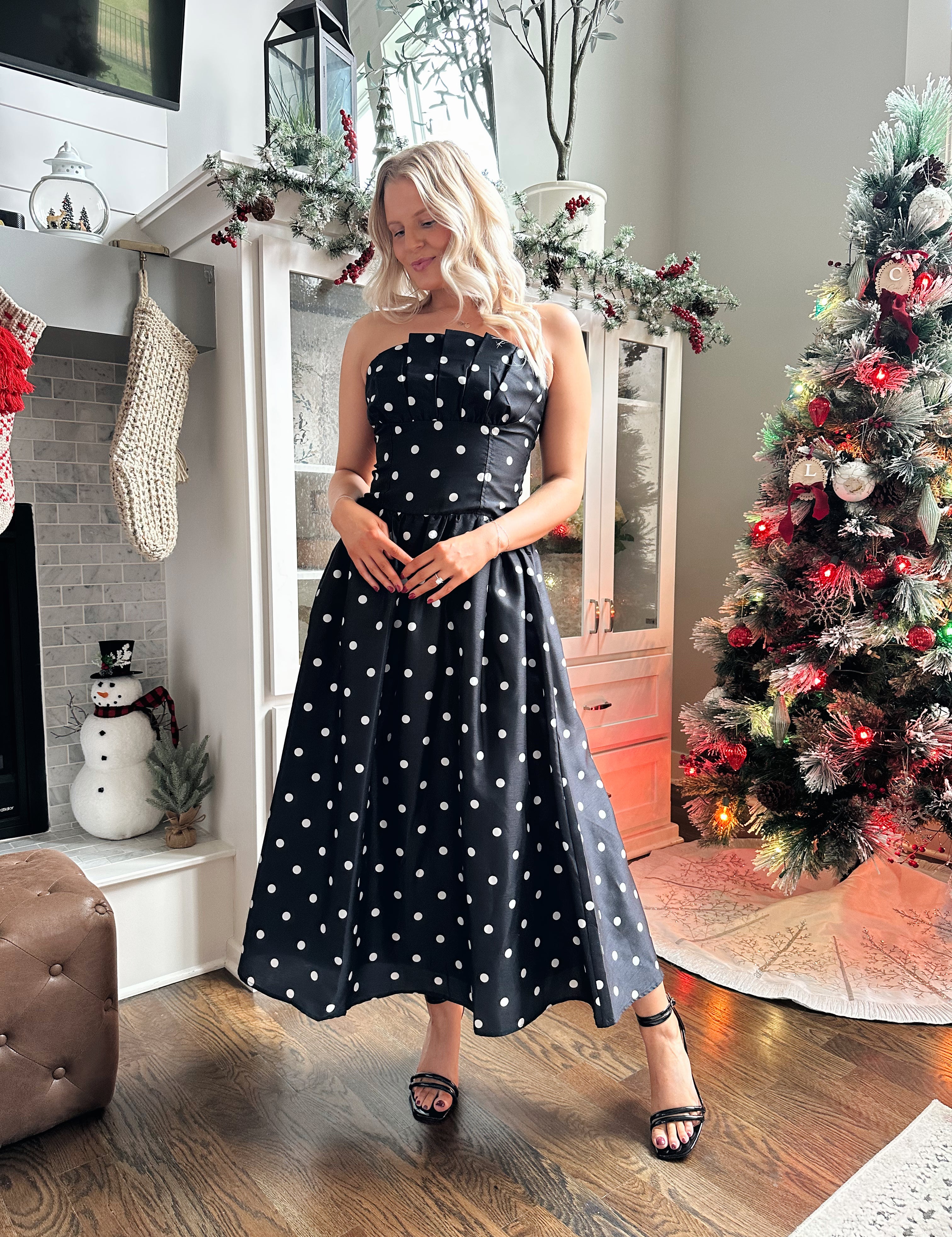 Woman wearing strapless black and white polka dot fit to flare midi dress. 