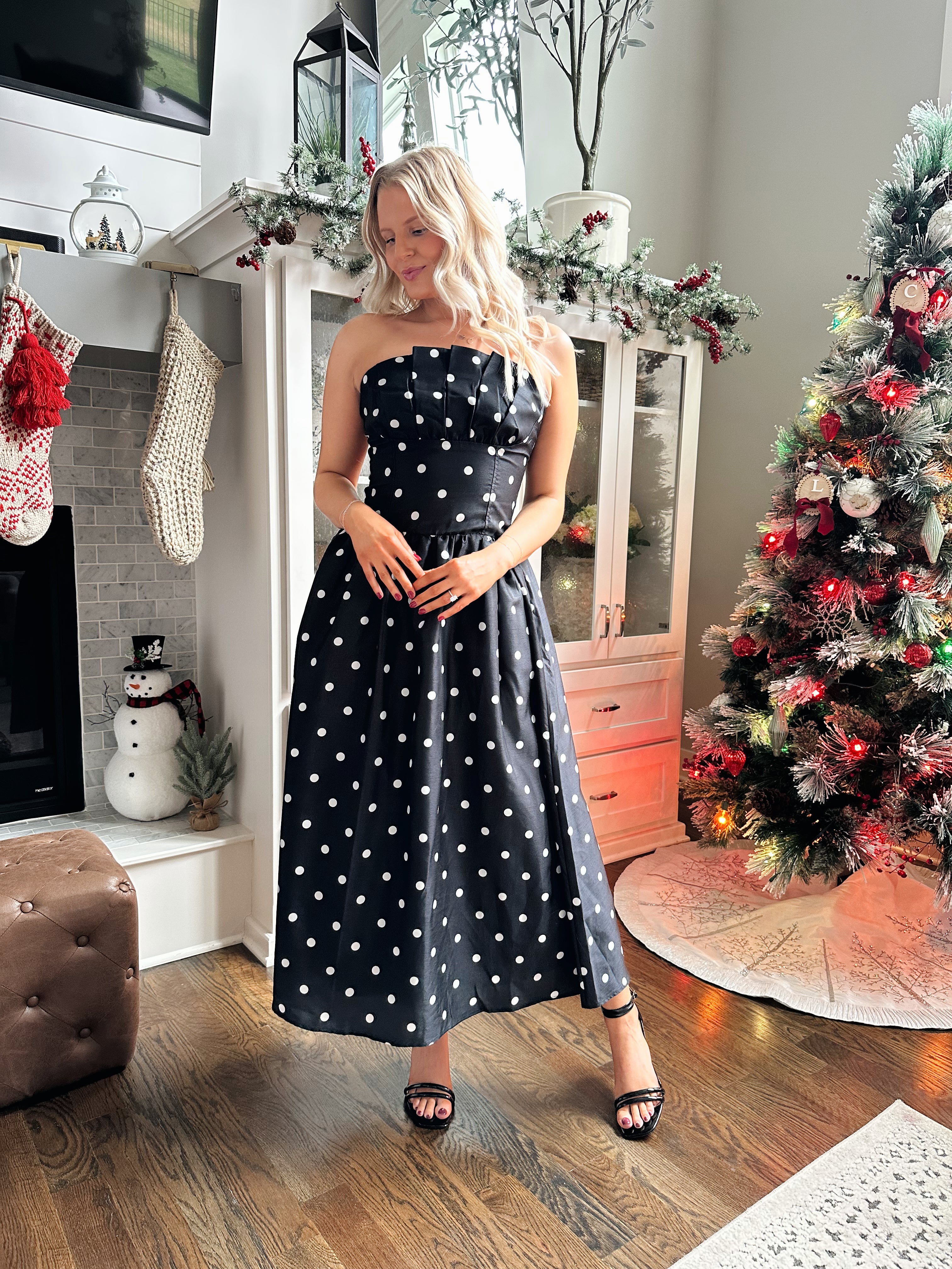 Woman wearing strapless black and white polka dot fit to flare midi dress. 