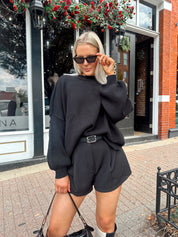 Woman wearing black knit oversized crewneck sweater with black shorts.