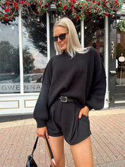 Woman wearing black knit oversized crewneck sweater with black shorts.