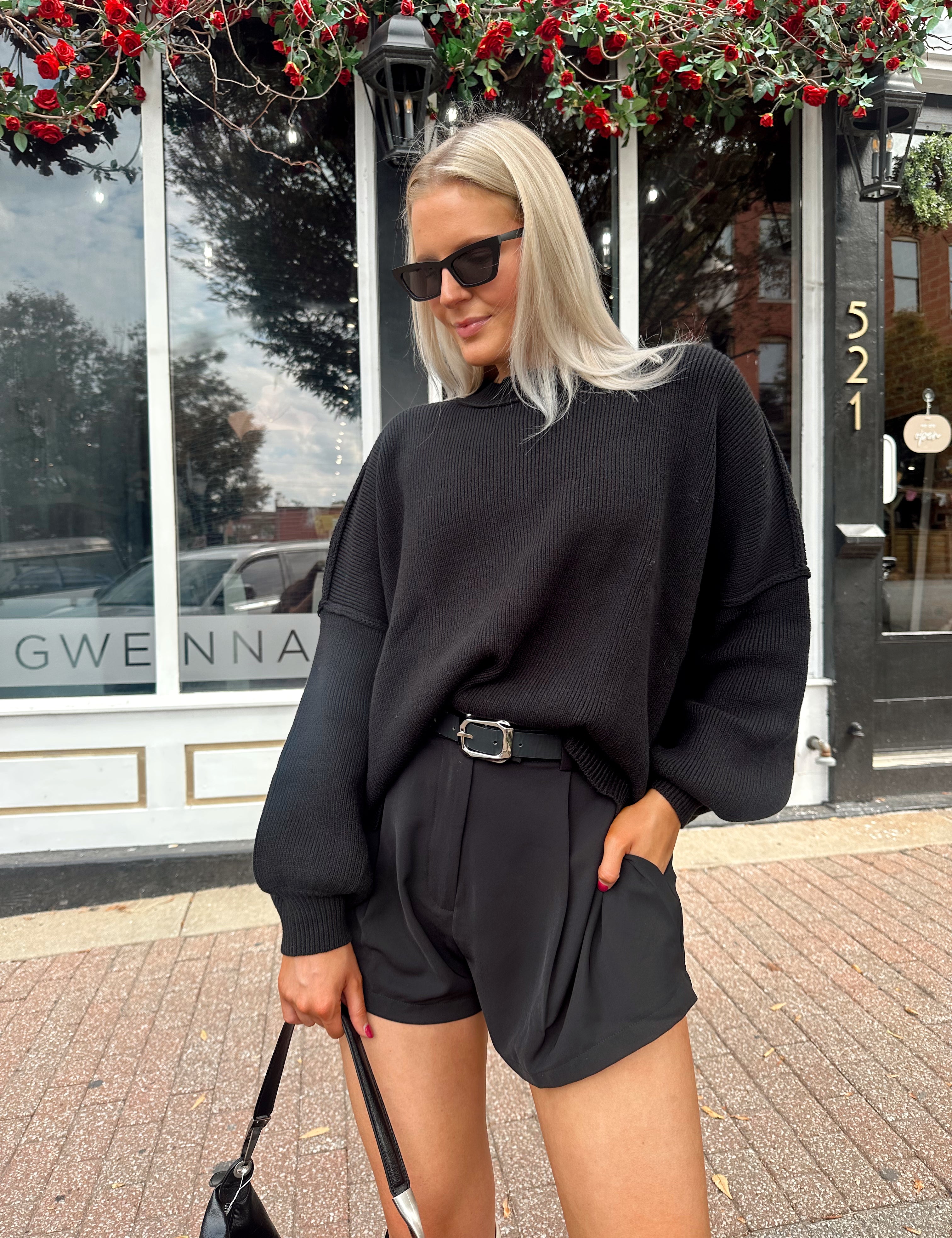 Woman wearing black knit oversized crewneck sweater with black shorts.