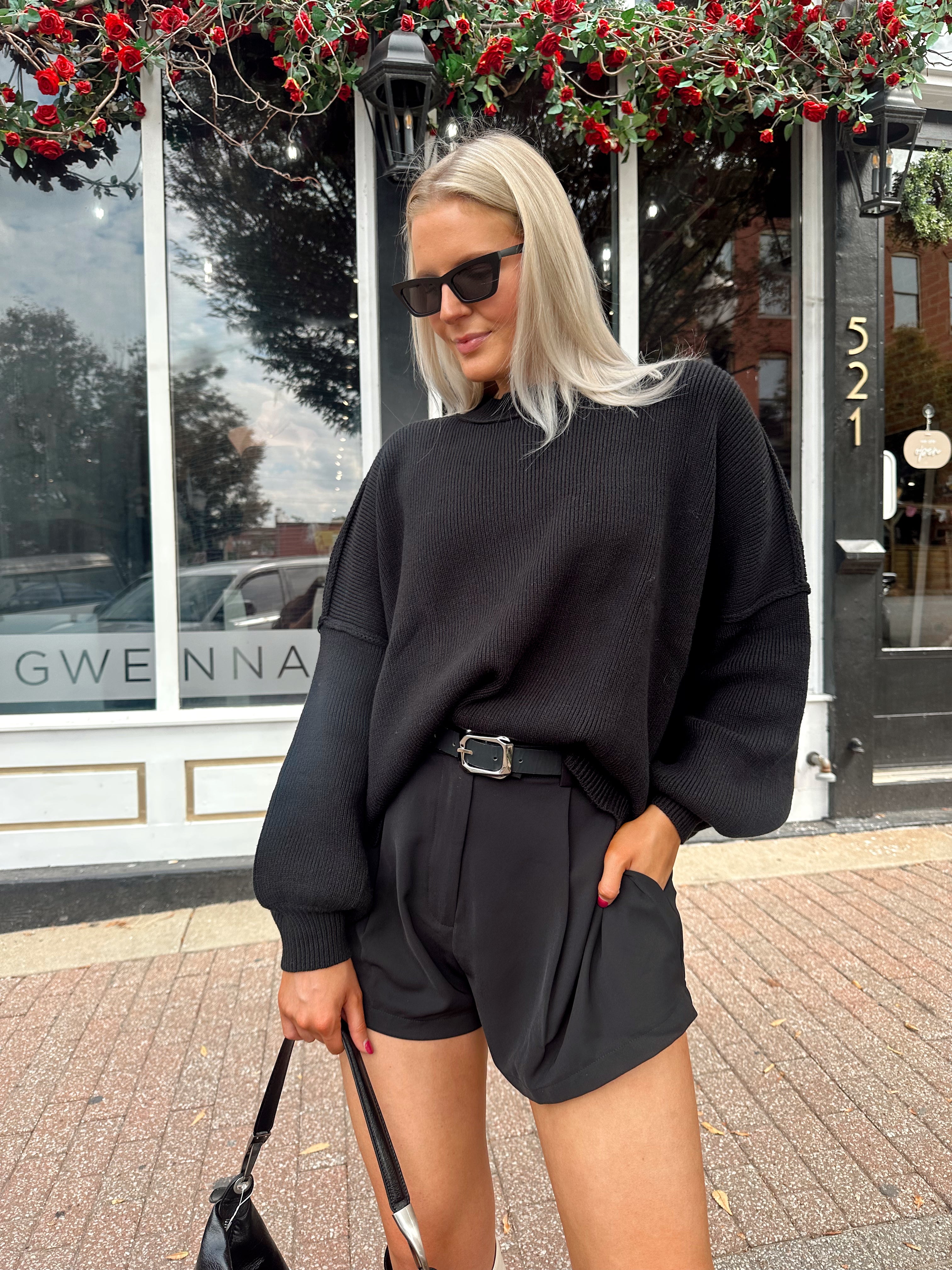 Woman wearing black knit oversized crewneck sweater with black shorts.