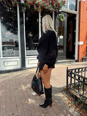 Woman wearing black knit oversized crewneck sweater with black shorts.