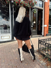 Woman wearing black knit oversized crewneck sweater with black shorts.