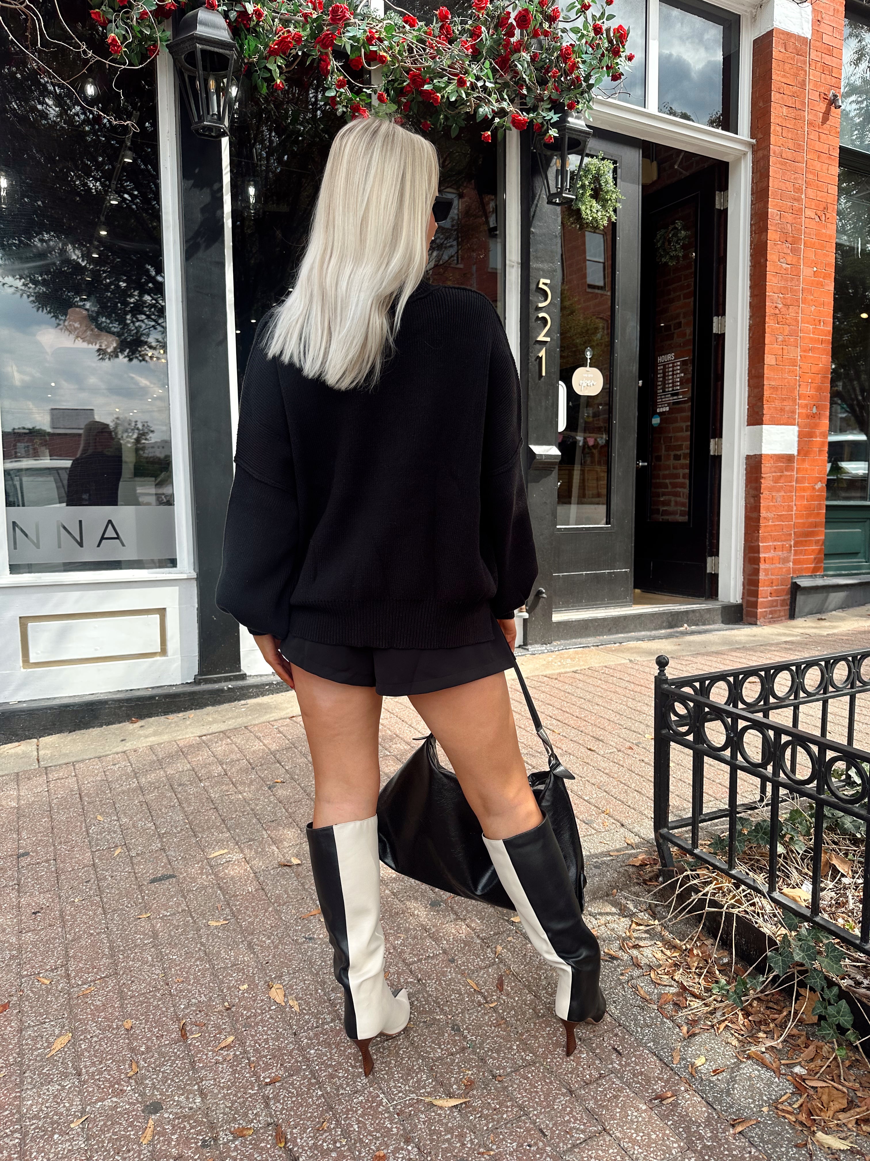 Woman wearing black knit oversized crewneck sweater with black shorts.