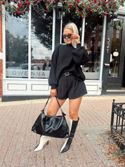 Woman wearing black knit oversized crewneck sweater with black shorts.