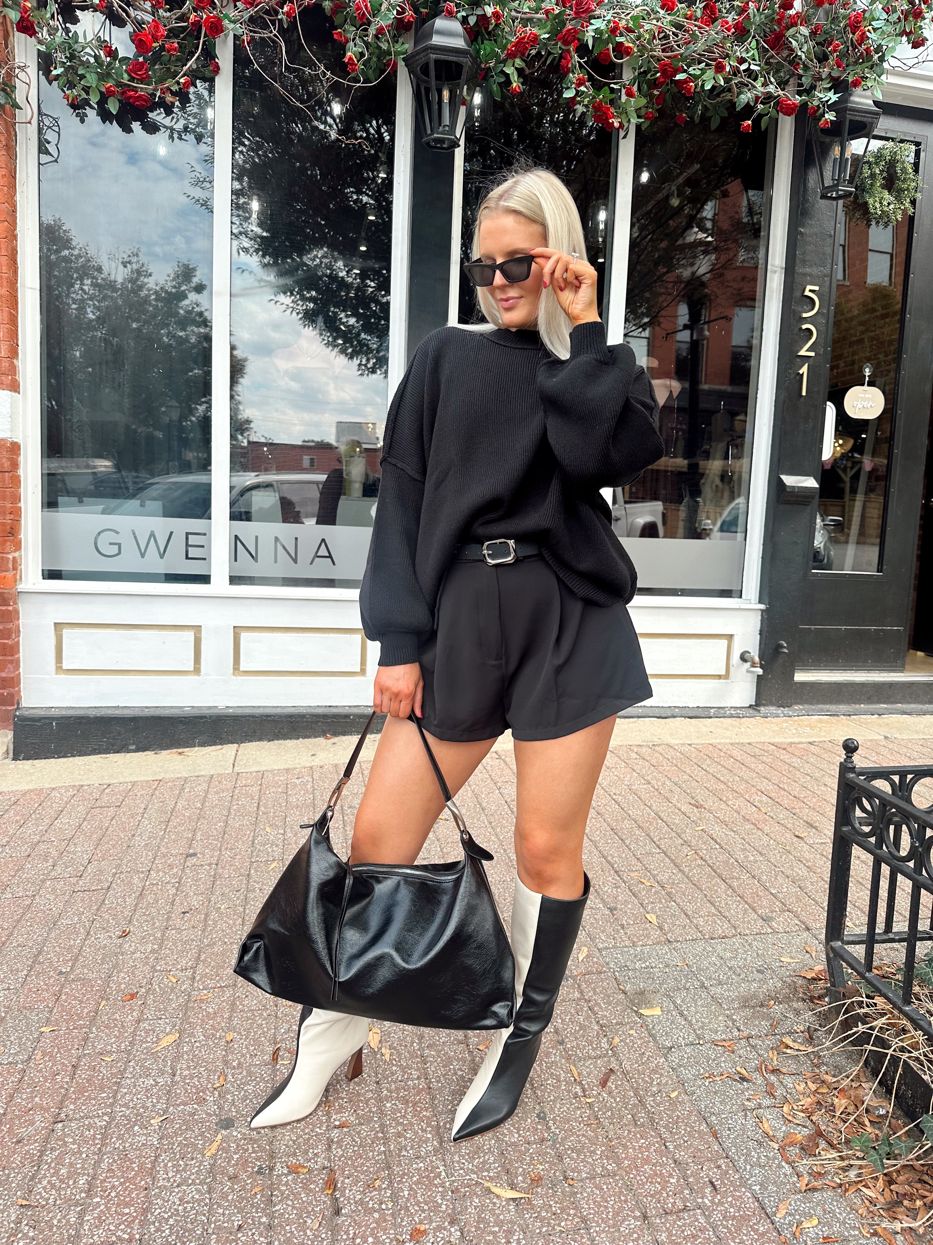 Woman wearing black knit oversized crewneck sweater with black shorts.