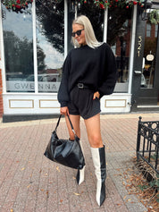 Woman wearing black knit oversized crewneck sweater with black shorts.