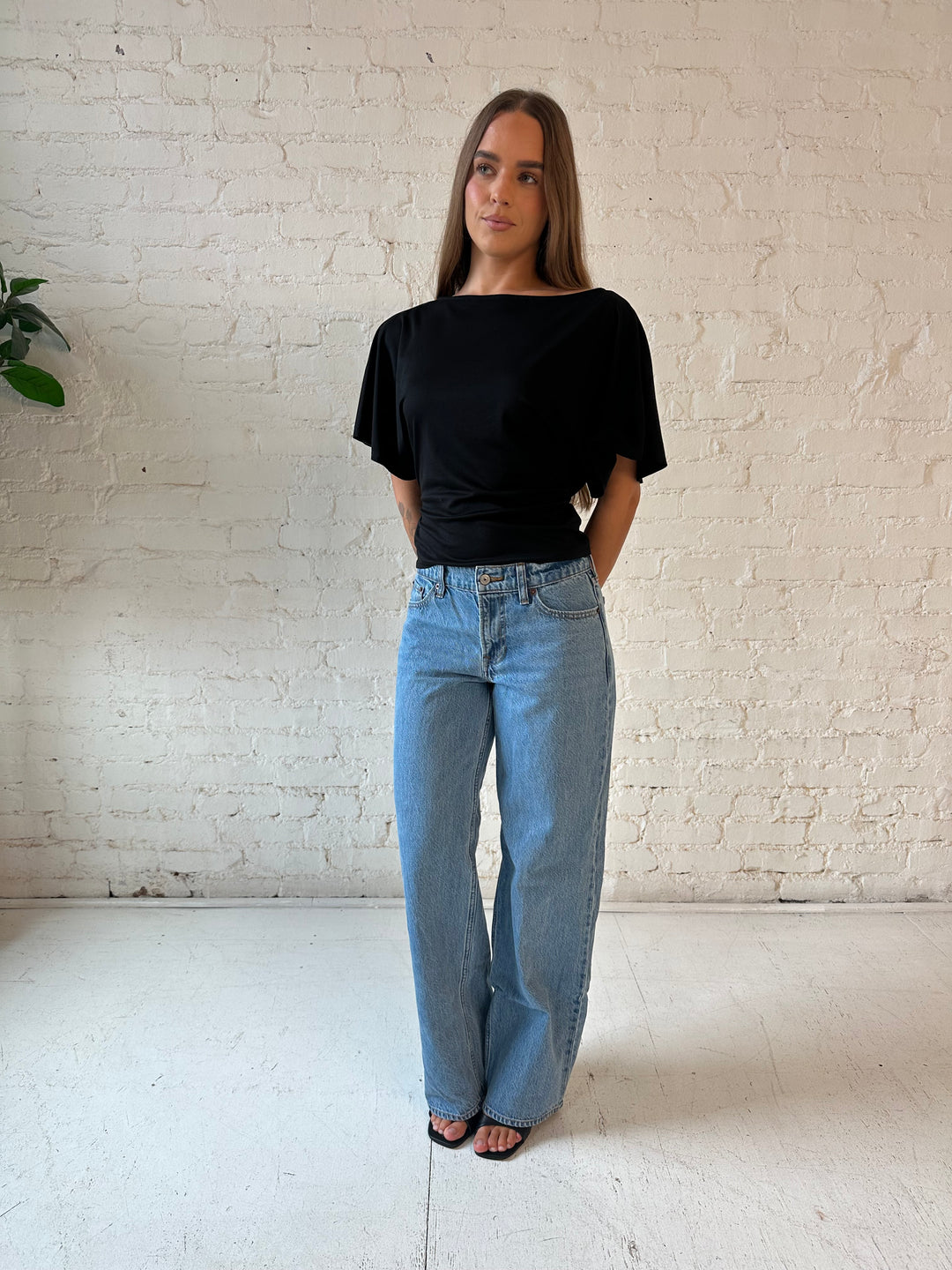 Woman wearing black short sleeve tie back top with medium wash jeans. 