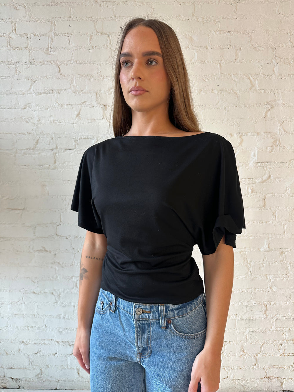 Woman wearing black short sleeve tie back top with medium wash jeans. 