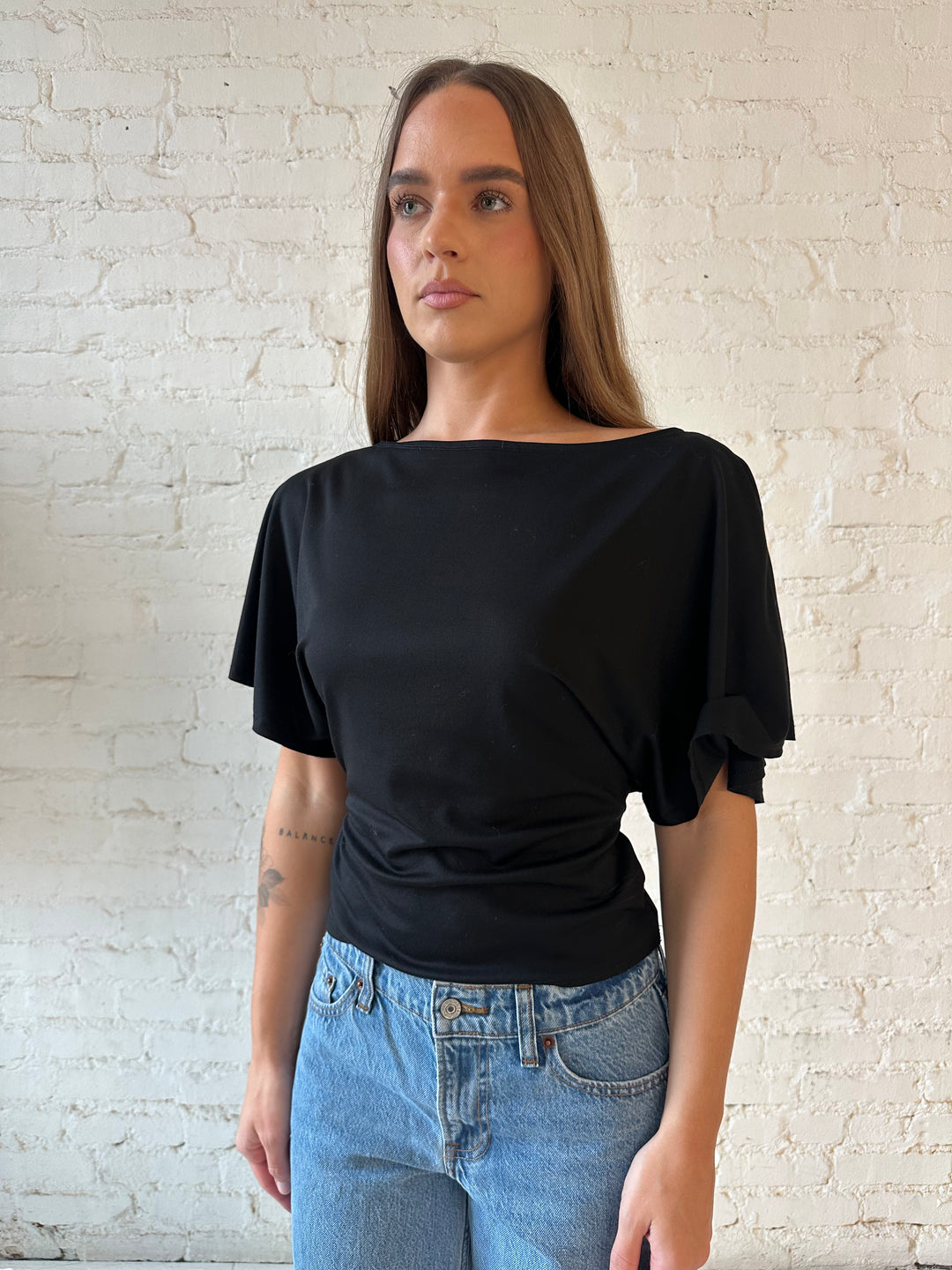 Woman wearing black short sleeve tie back top with medium wash jeans. 