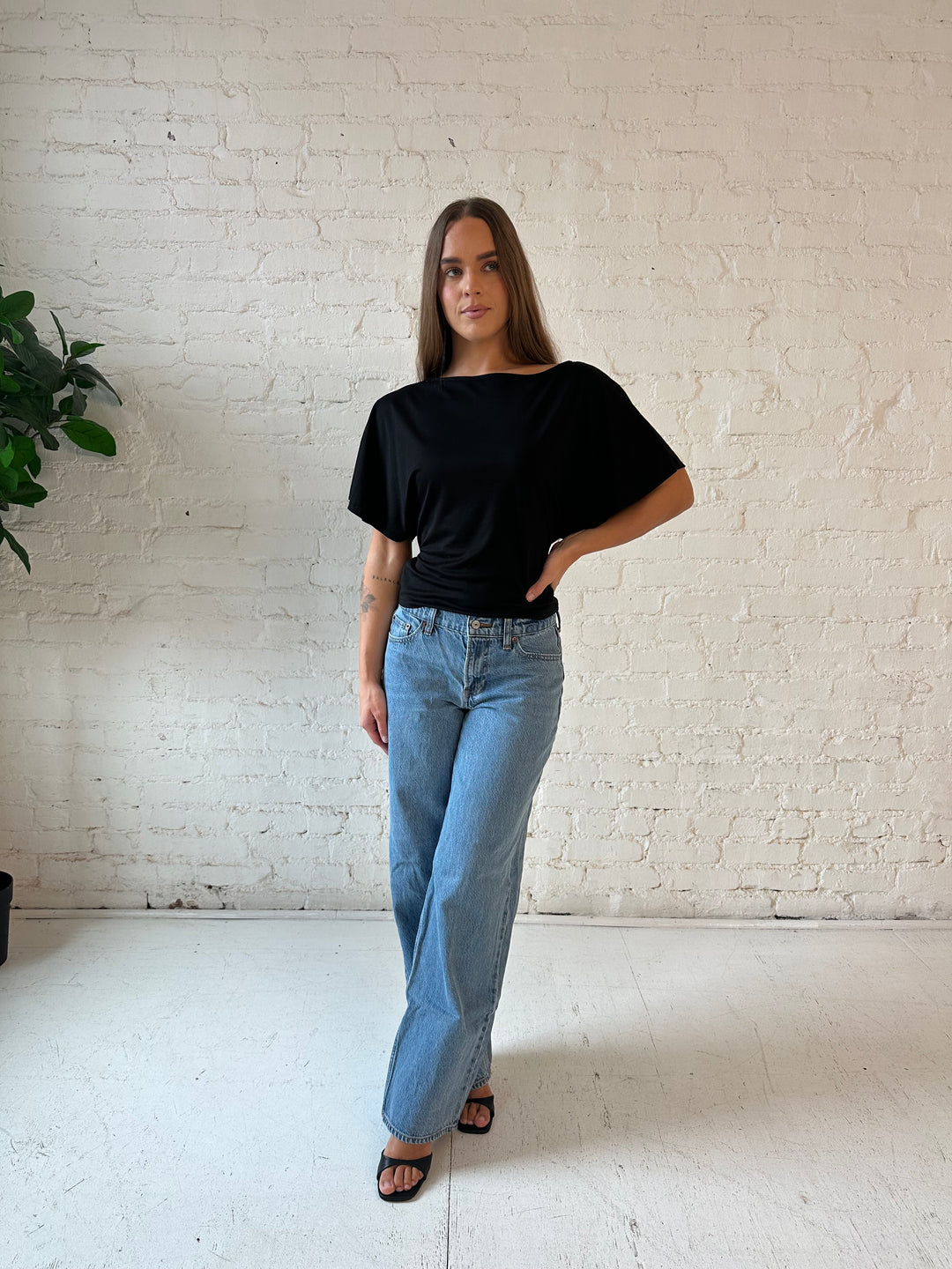 Woman wearing black short sleeve tie back top with medium wash jeans. 