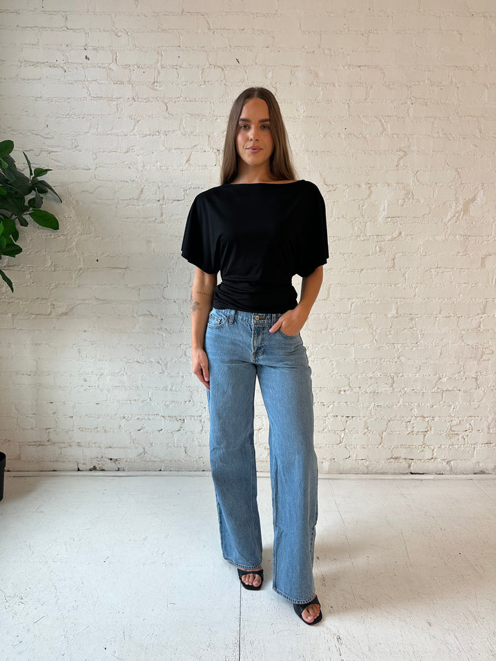 Woman wearing black short sleeve tie back top with medium wash jeans. 