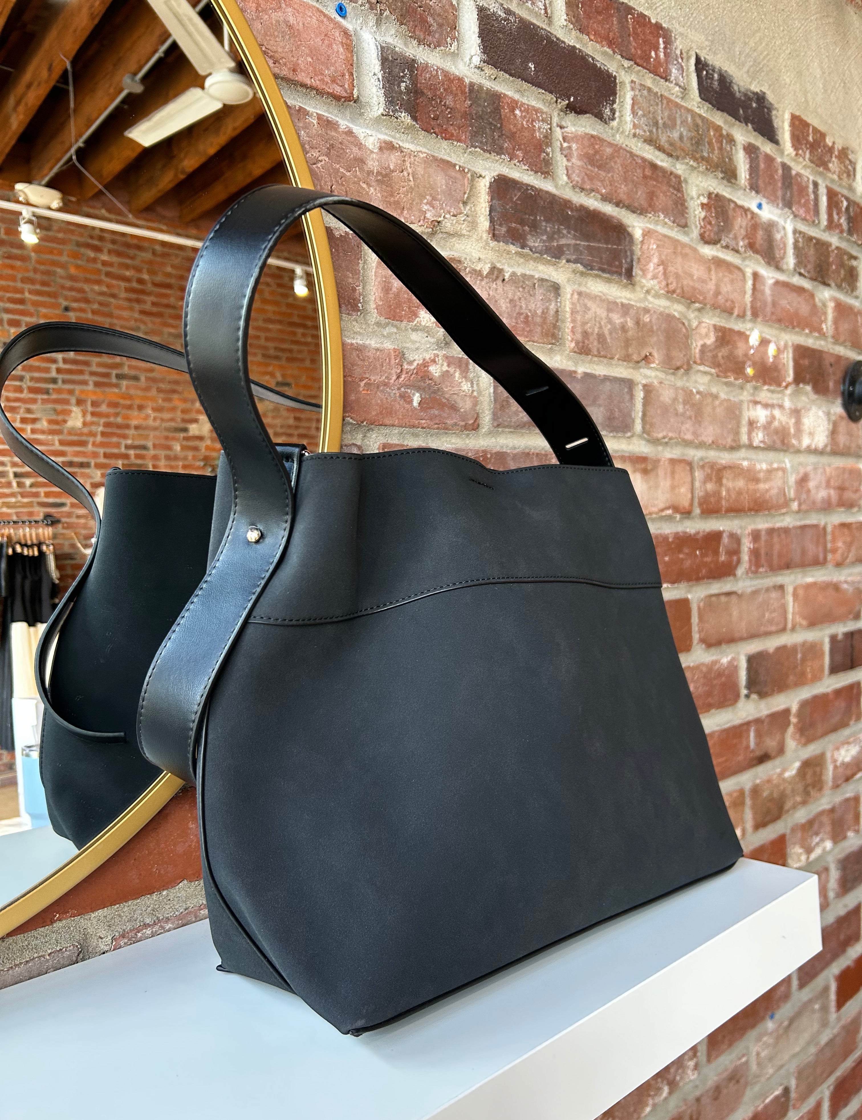 Black suede shoulder bag with adjustable leather strap and interior organizer pouch insert displayed in boutique setting.