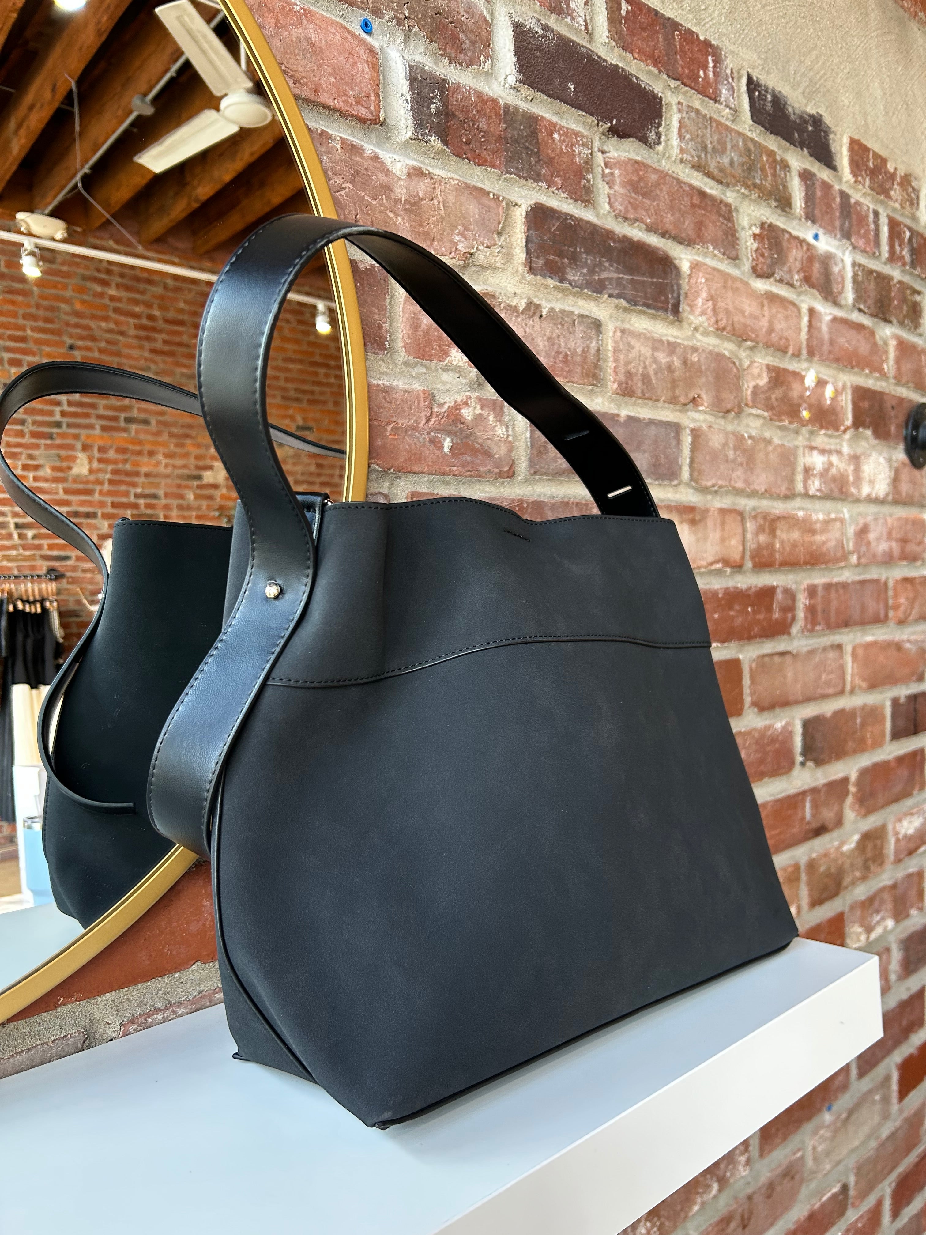 Black suede shoulder bag with adjustable leather strap and interior organizer pouch insert displayed in boutique setting.