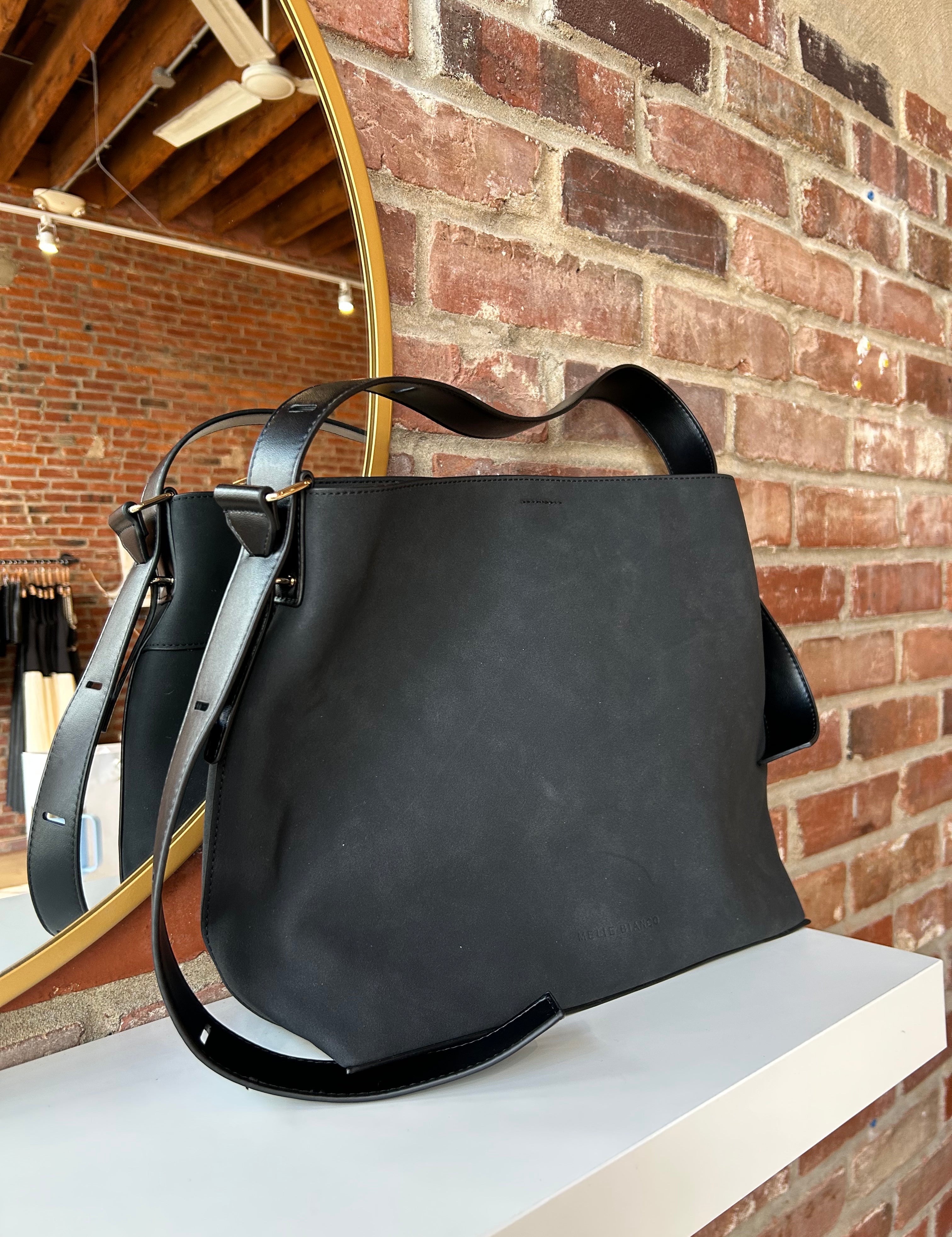 Black suede shoulder bag with adjustable leather strap and interior organizer pouch insert displayed in boutique setting.