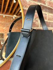 Black suede shoulder bag with adjustable leather strap and interior organizer pouch insert displayed in boutique setting.