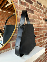 Black suede shoulder bag with adjustable leather strap and interior organizer pouch insert displayed in boutique setting.