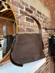 Espresso brown suede shoulder bag with adjustable strap and removable organizer pouch displayed on boutique shelf.