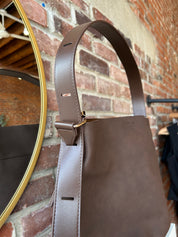 Espresso brown suede shoulder bag with adjustable strap and removable organizer pouch displayed on boutique shelf.