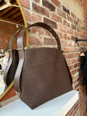 Espresso brown suede shoulder bag with adjustable strap and removable organizer pouch displayed on boutique shelf.
