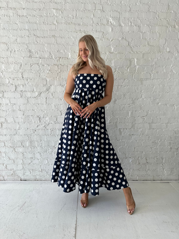 Woman wearing navy and white polka dot maxi dress with straight neckline and adjustable straps.
