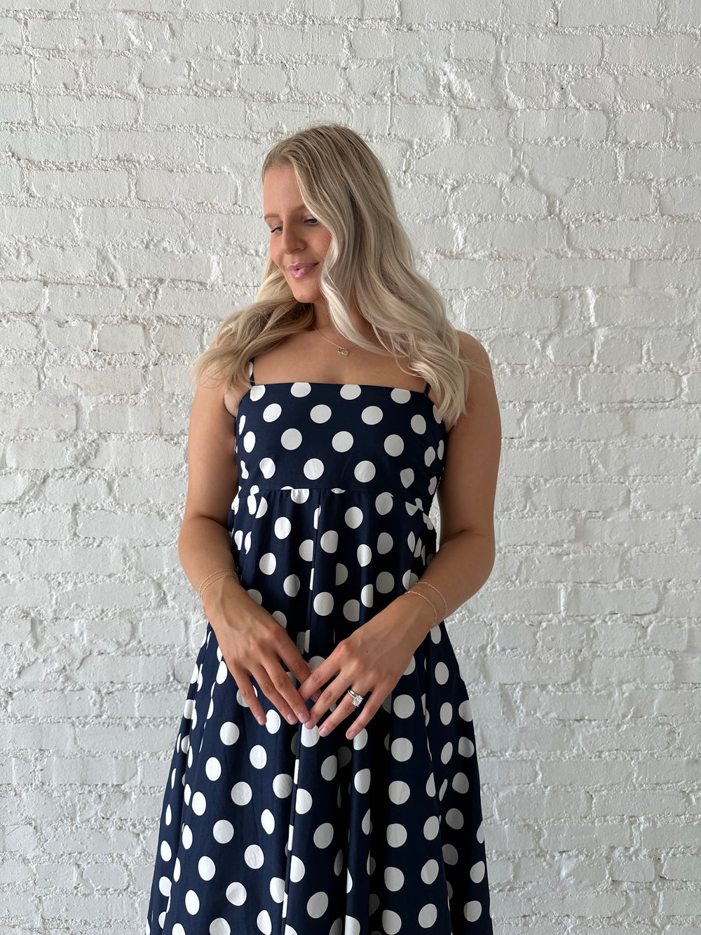 Woman wearing navy and white polka dot maxi dress with straight neckline and adjustable straps.