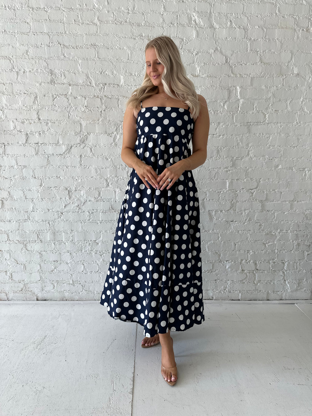 Woman wearing navy and white polka dot maxi dress with straight neckline and adjustable straps.