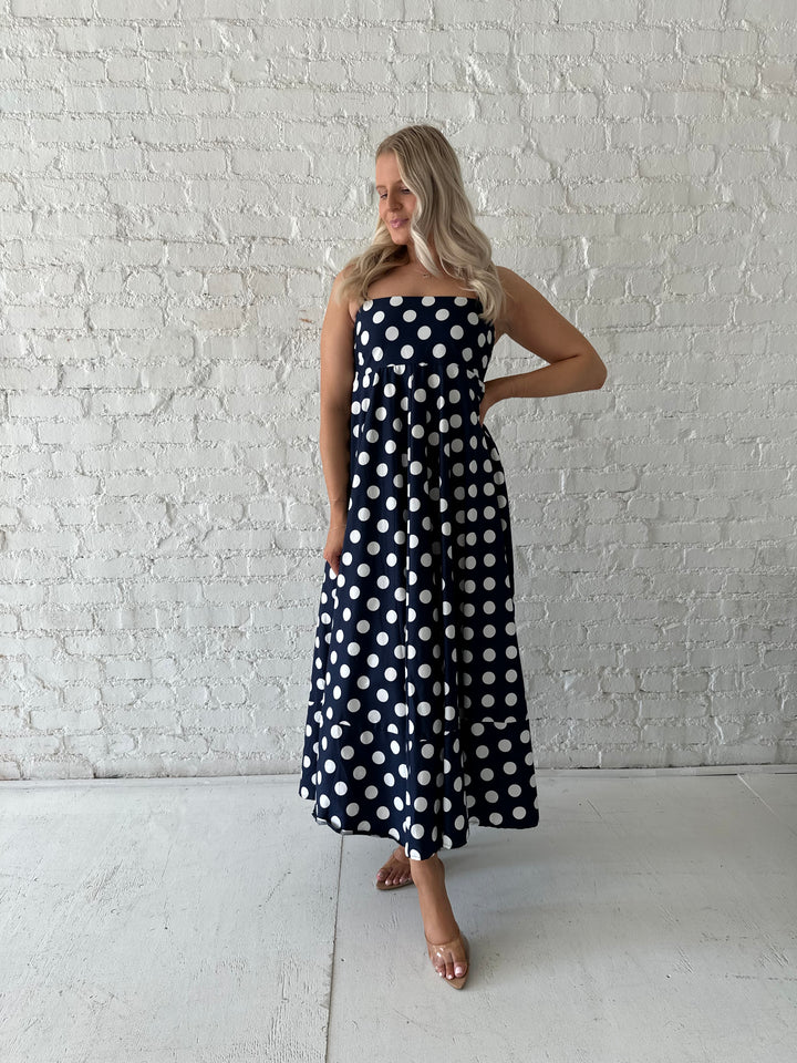 Woman wearing navy and white polka dot maxi dress with straight neckline and adjustable straps.
