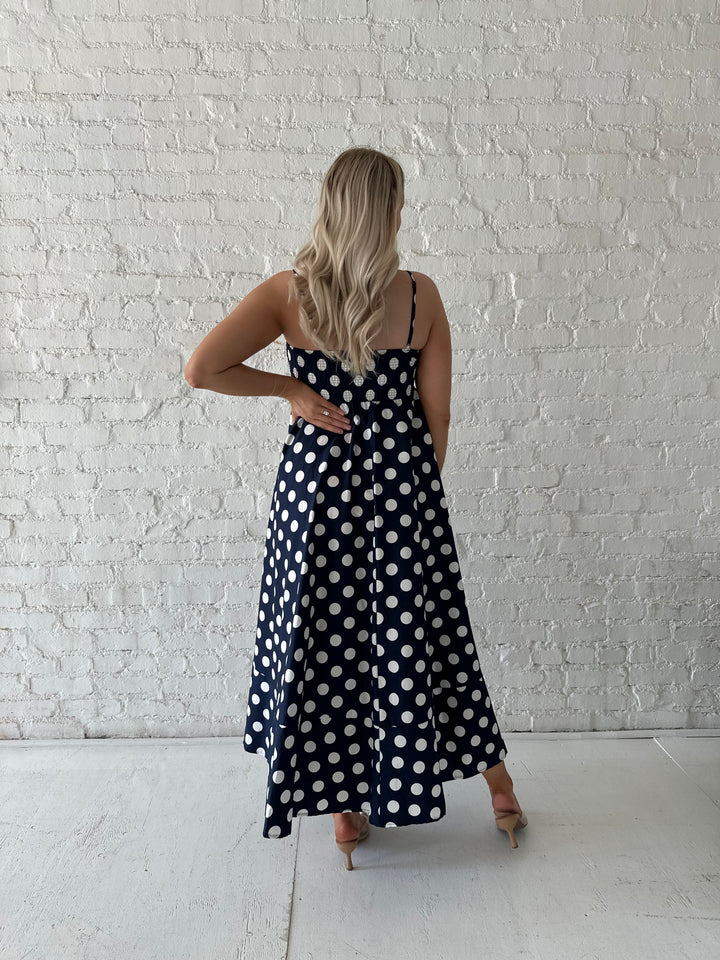 Woman wearing navy and white polka dot maxi dress with straight neckline and adjustable straps.