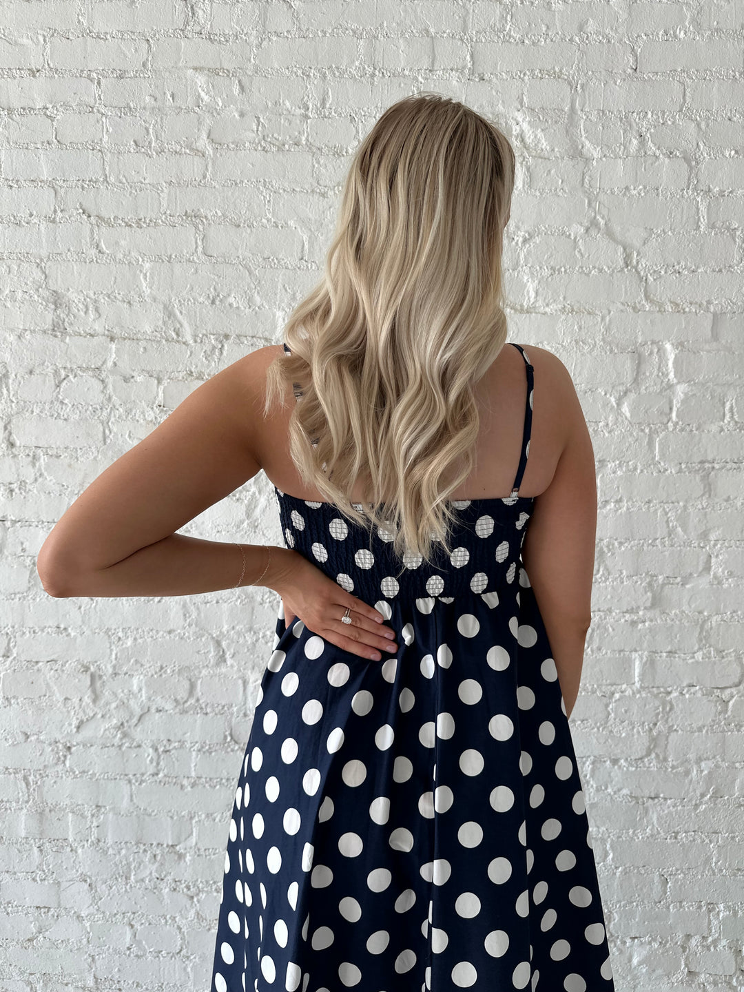 Woman wearing navy and white polka dot maxi dress with straight neckline and adjustable straps.