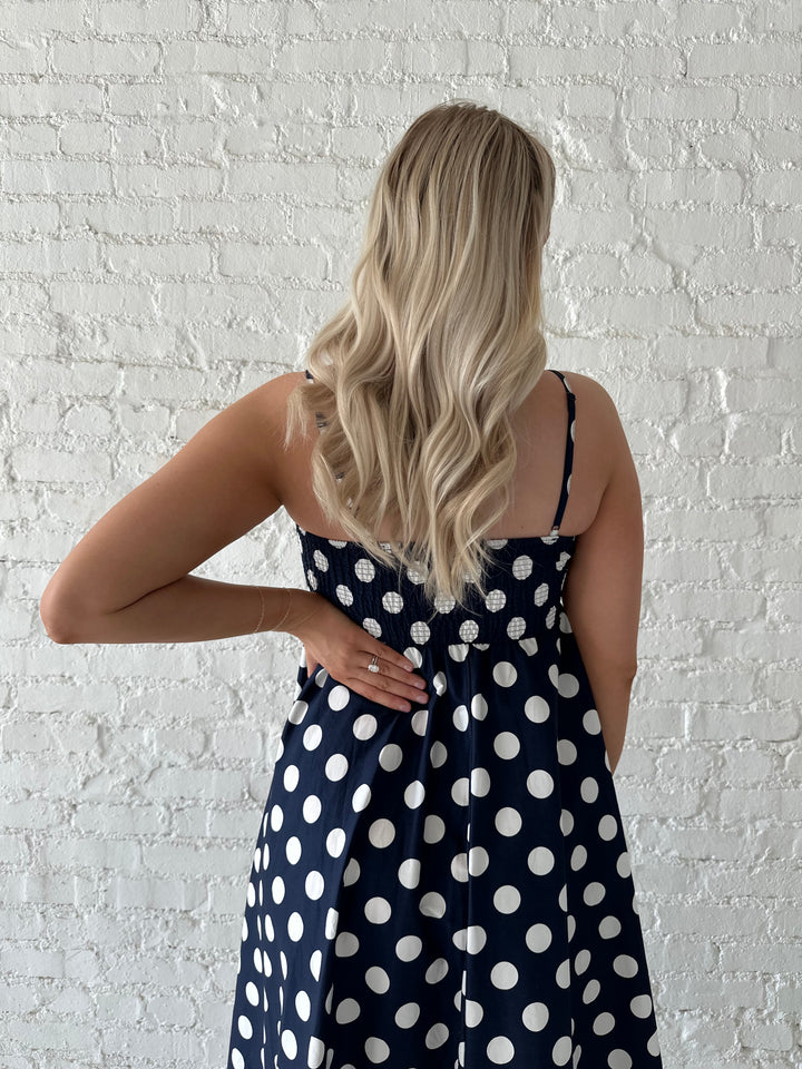 Woman wearing navy and white polka dot maxi dress with straight neckline and adjustable straps.