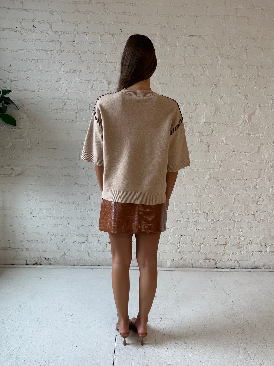 Woman wearing beige colored sweater with contrast stitch sleeve detail and cognac leather mini skirt. 