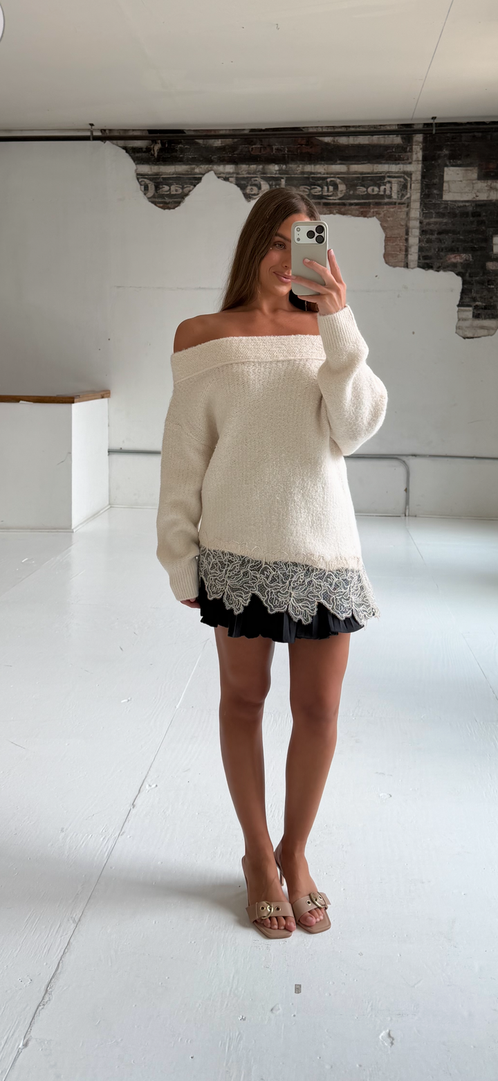 Woman wearing charcoal gray pleated mini skort with cream off the shoulder sweater. 