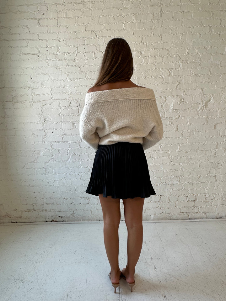 Woman wearing charcoal gray pleated mini skort with cream off the shoulder sweater. 