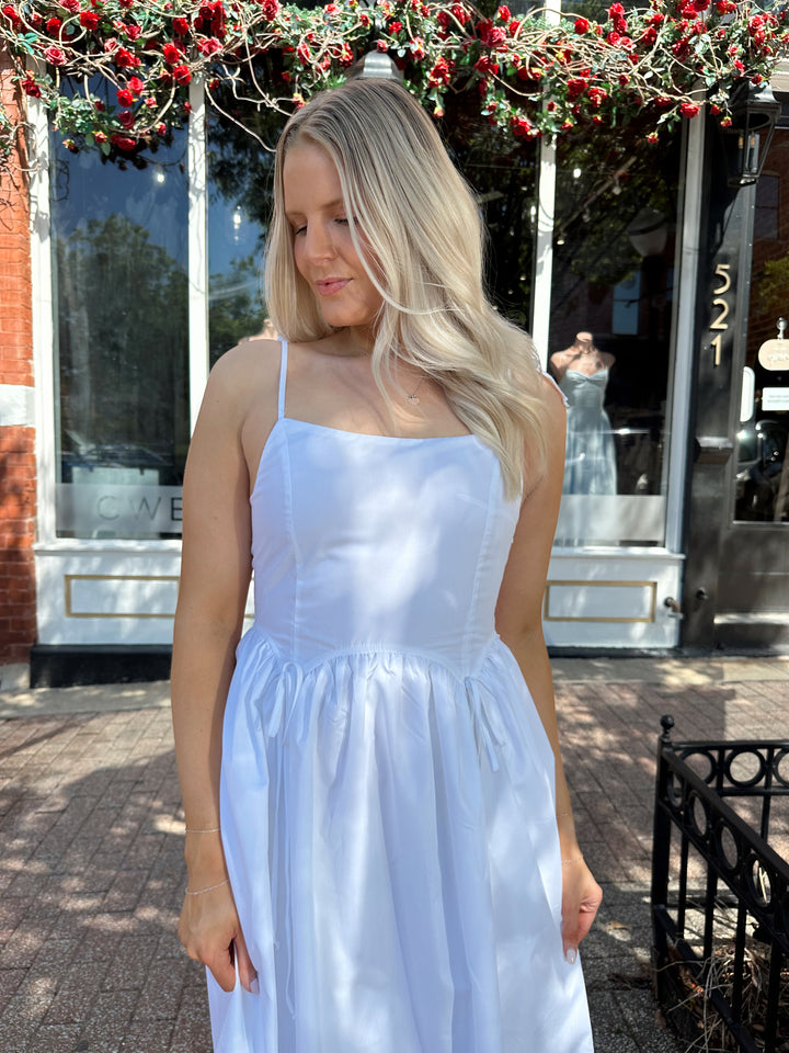 Woman wearing white midi dress with front tie detail, and self tie straps.