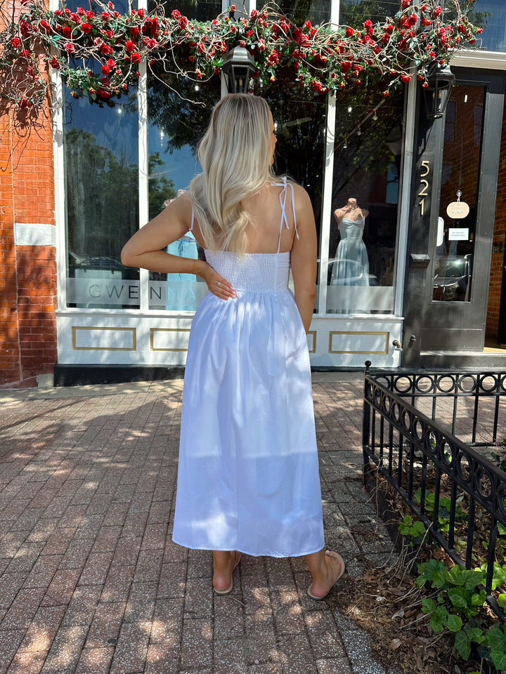 Woman wearing white midi dress with front tie detail, and self tie straps.