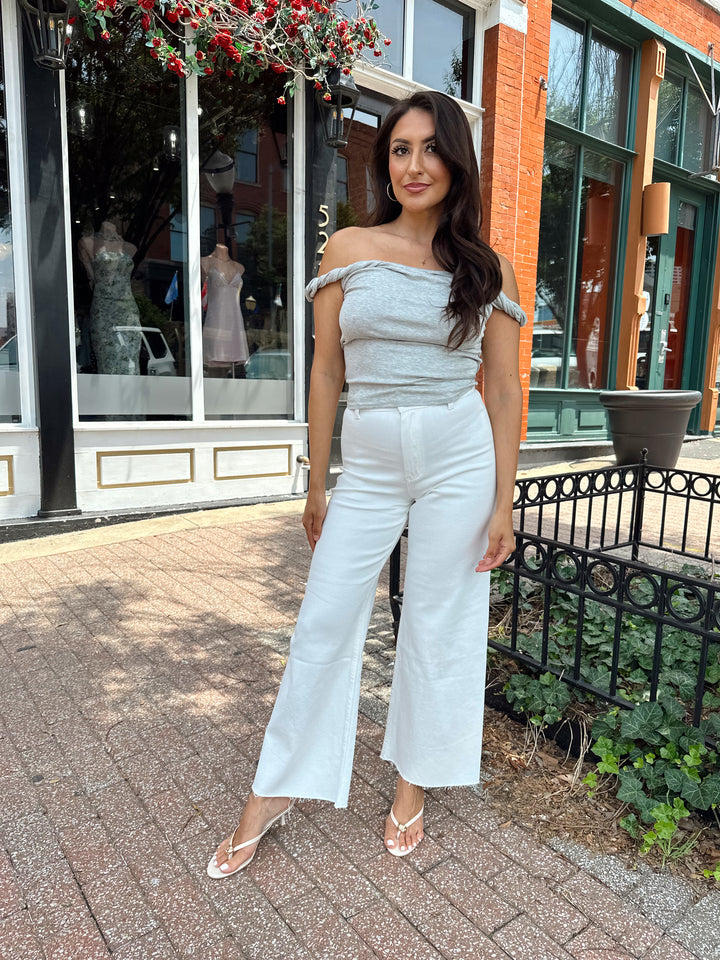 Woman wearing grey off the shoulder twist top with cream colored, wide leg jean.