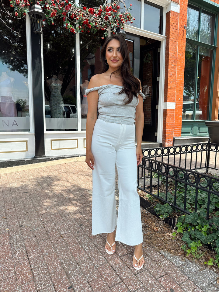 Woman wearing grey off the shoulder twist top with cream colored, wide leg jean.