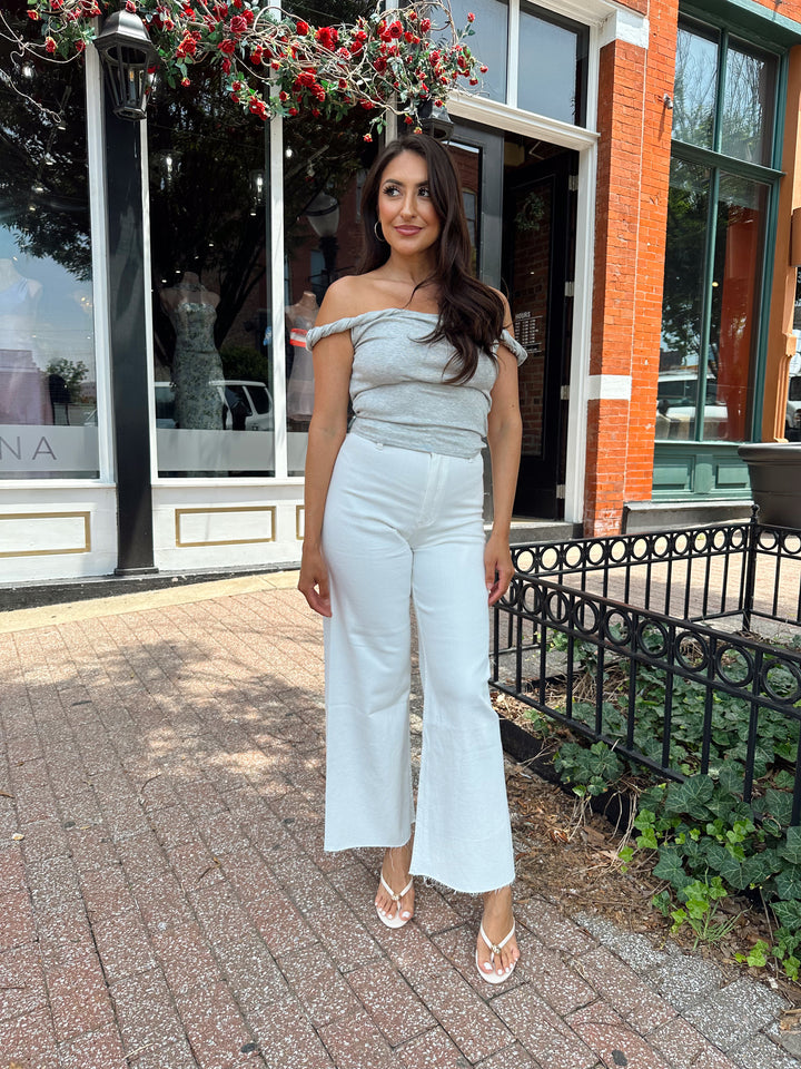 Woman wearing grey off the shoulder twist top with cream colored, wide leg jean.
