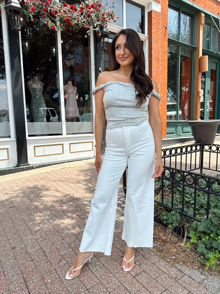 Woman wearing grey off the shoulder twist top with cream colored, wide leg jean.