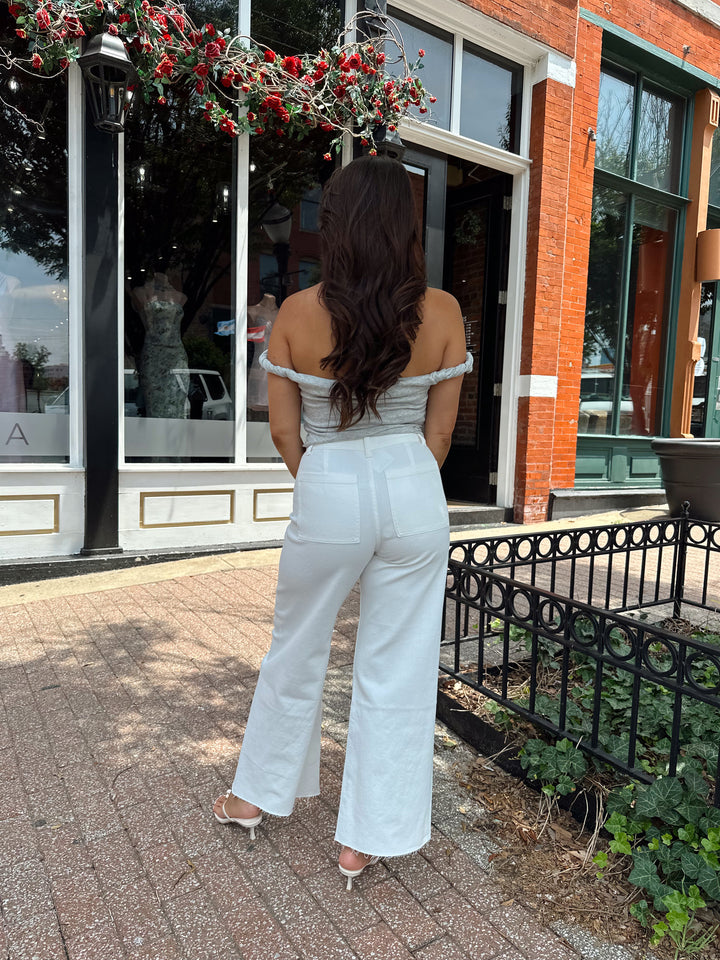 Woman wearing grey off the shoulder twist top with cream colored, wide leg jean.