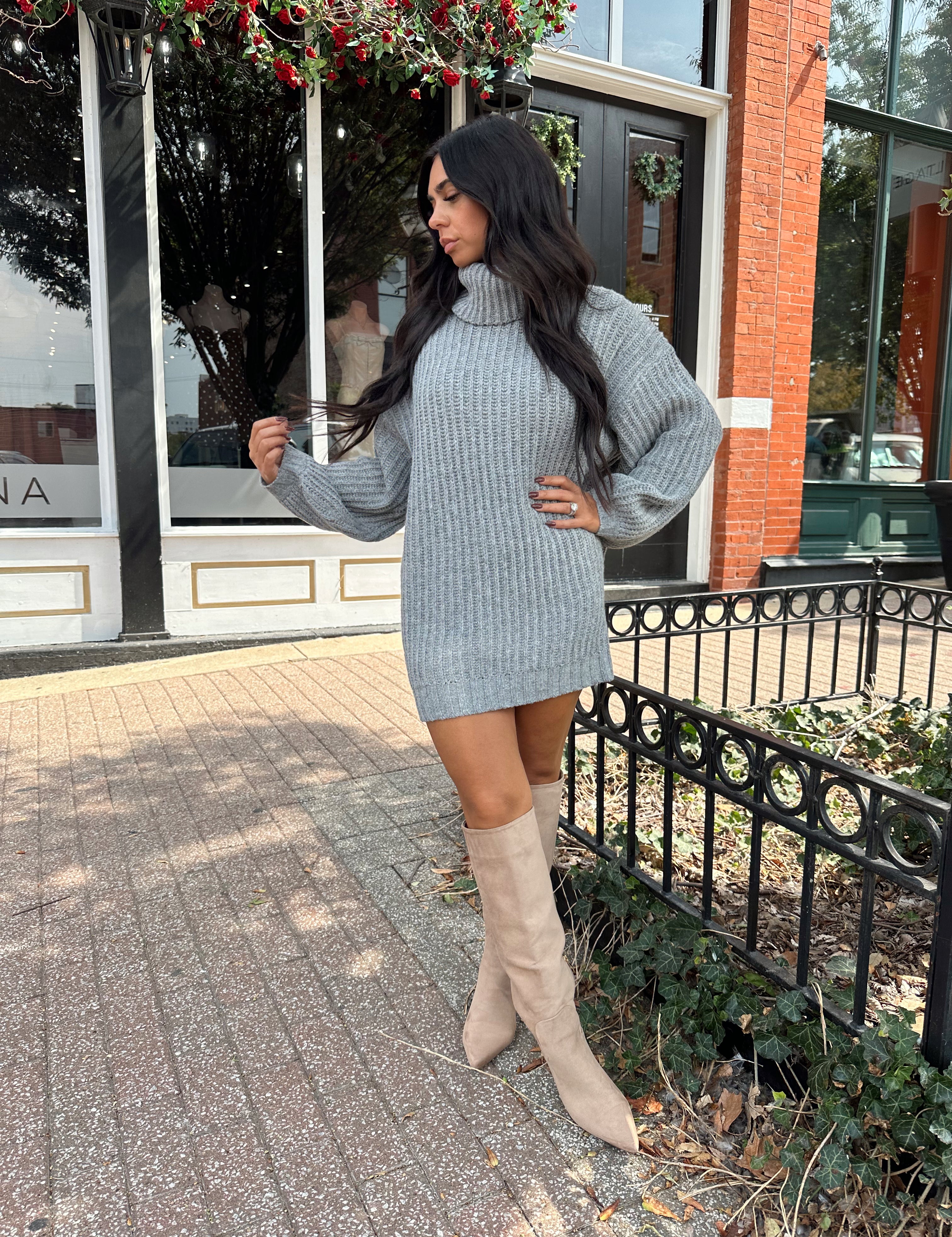 Woman wearing grey knit oversized turtle neck sweater dress with suede knee boots.