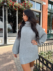 Woman wearing grey knit oversized turtle neck sweater dress with suede knee boots.