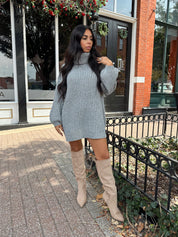 Woman wearing grey knit oversized turtle neck sweater dress with suede knee boots.
