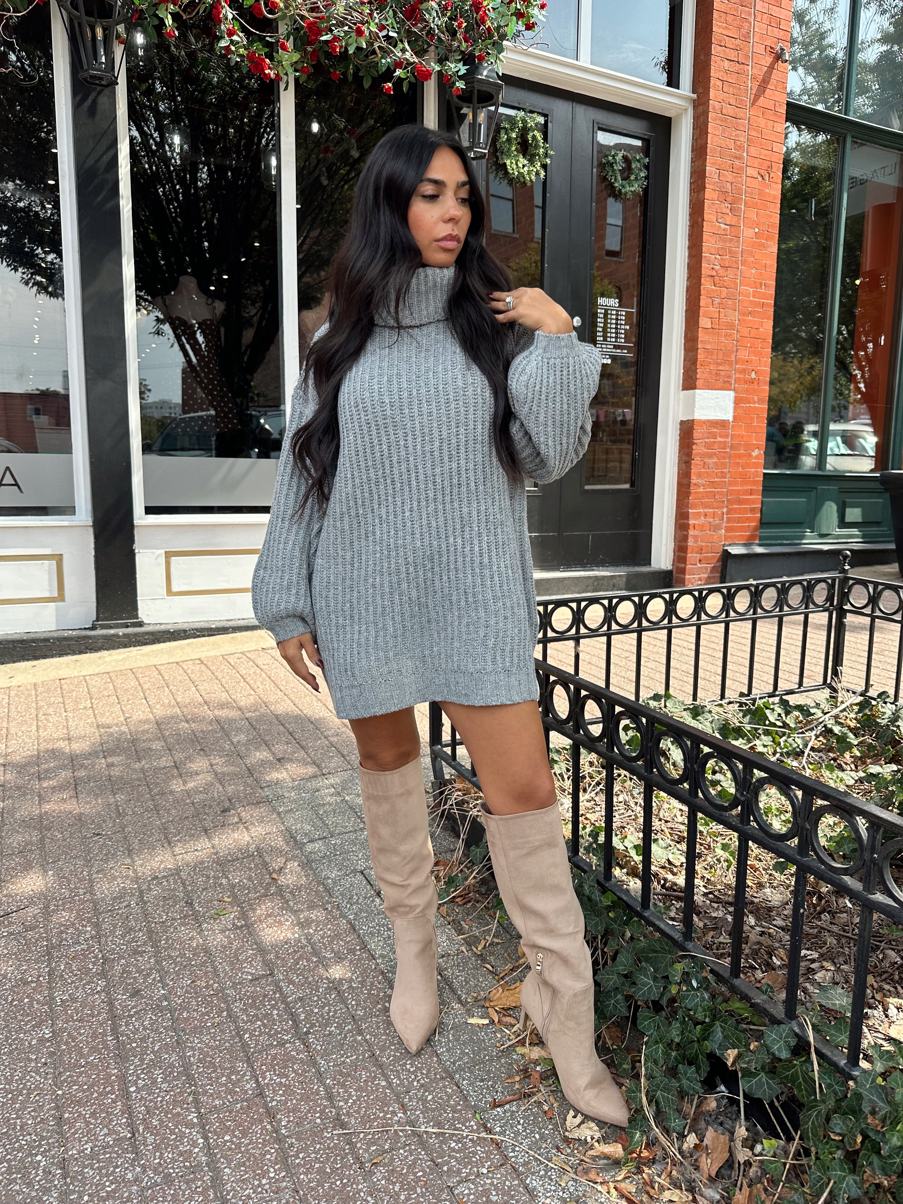 Woman wearing grey knit oversized turtle neck sweater dress with suede knee boots.