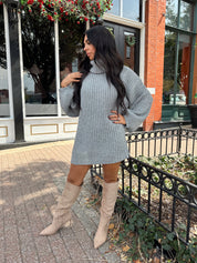 Woman wearing grey knit oversized turtle neck sweater dress with suede knee boots.